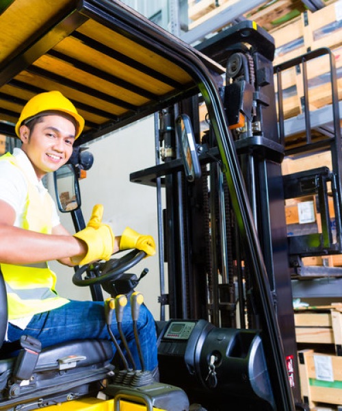 Happy warehouse worker operating a forklift for material handling, surrounded by stocked shelves in an organized warehouse environment