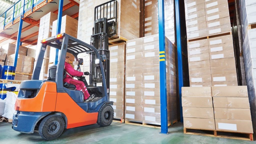 Warehouse worker operating forklift for double stacking pallets with cardboard boxes in a well-organized storage facility