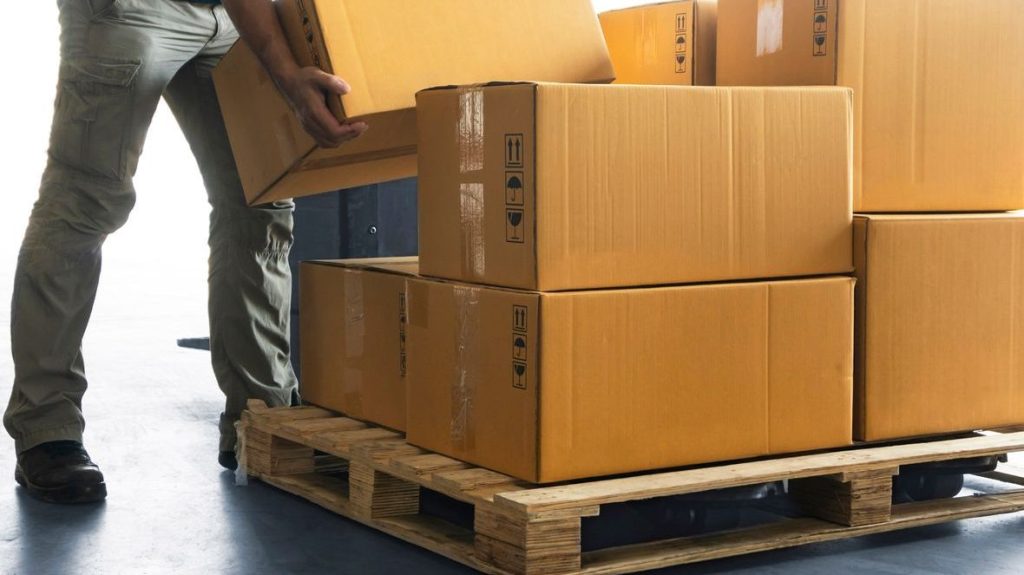 Worker demonstrating how to stack a pallet with uniform cardboard boxes in a warehouse, showcasing proper technique for balance and space utilization